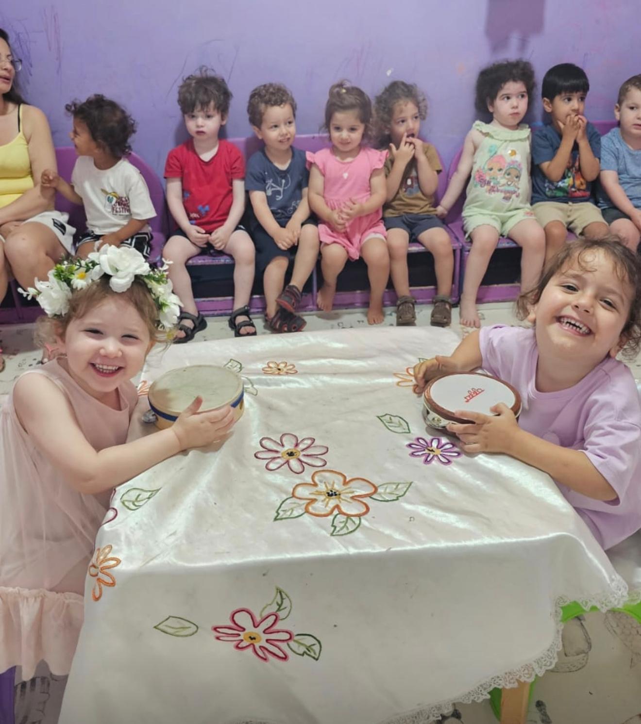 שתי ילדות מחייכות מנגנות בתופים בגן שקד